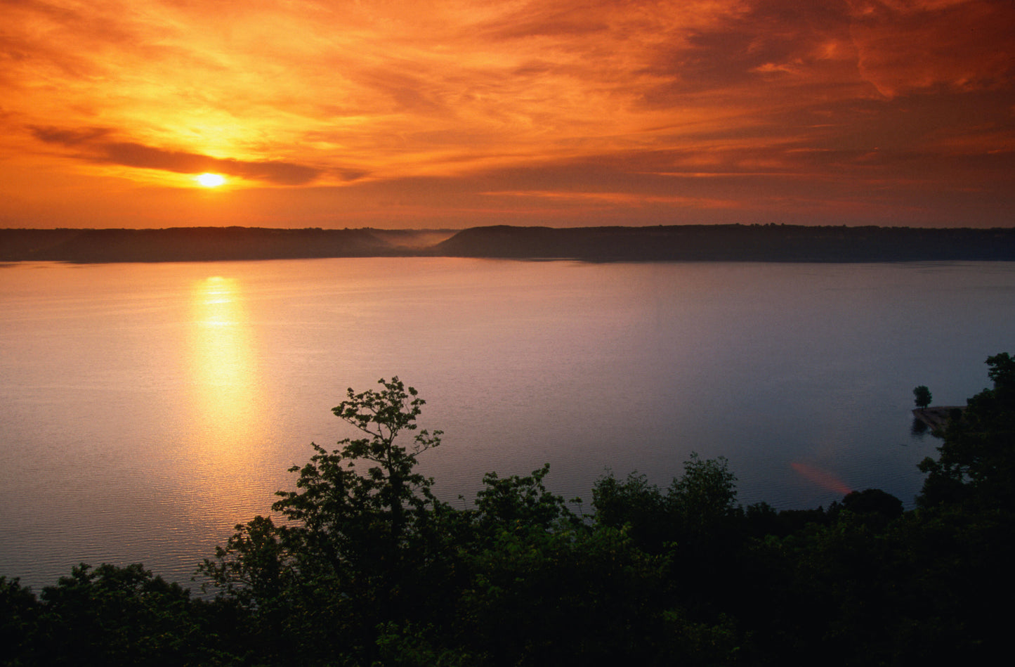 Sun sets over a large body of water surrounded by land and vegetation. Hydrogeology image.