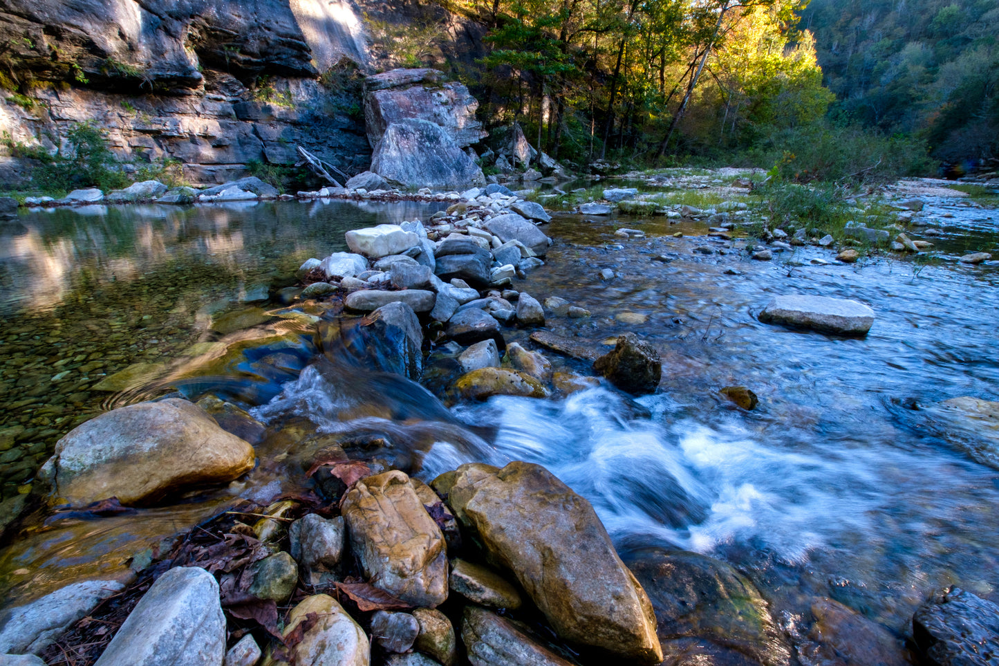 Water rushes over rocks in a riverbed surrounded by trees. Archaeology & Fluvial Landscapes image.