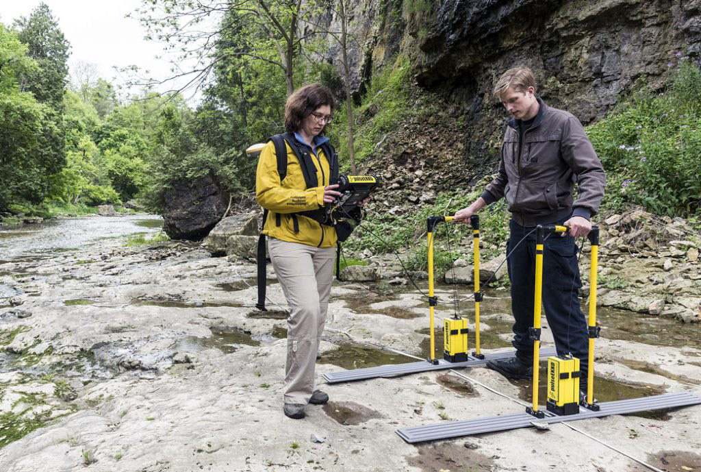 Two people with equipment in a natural setting near a river