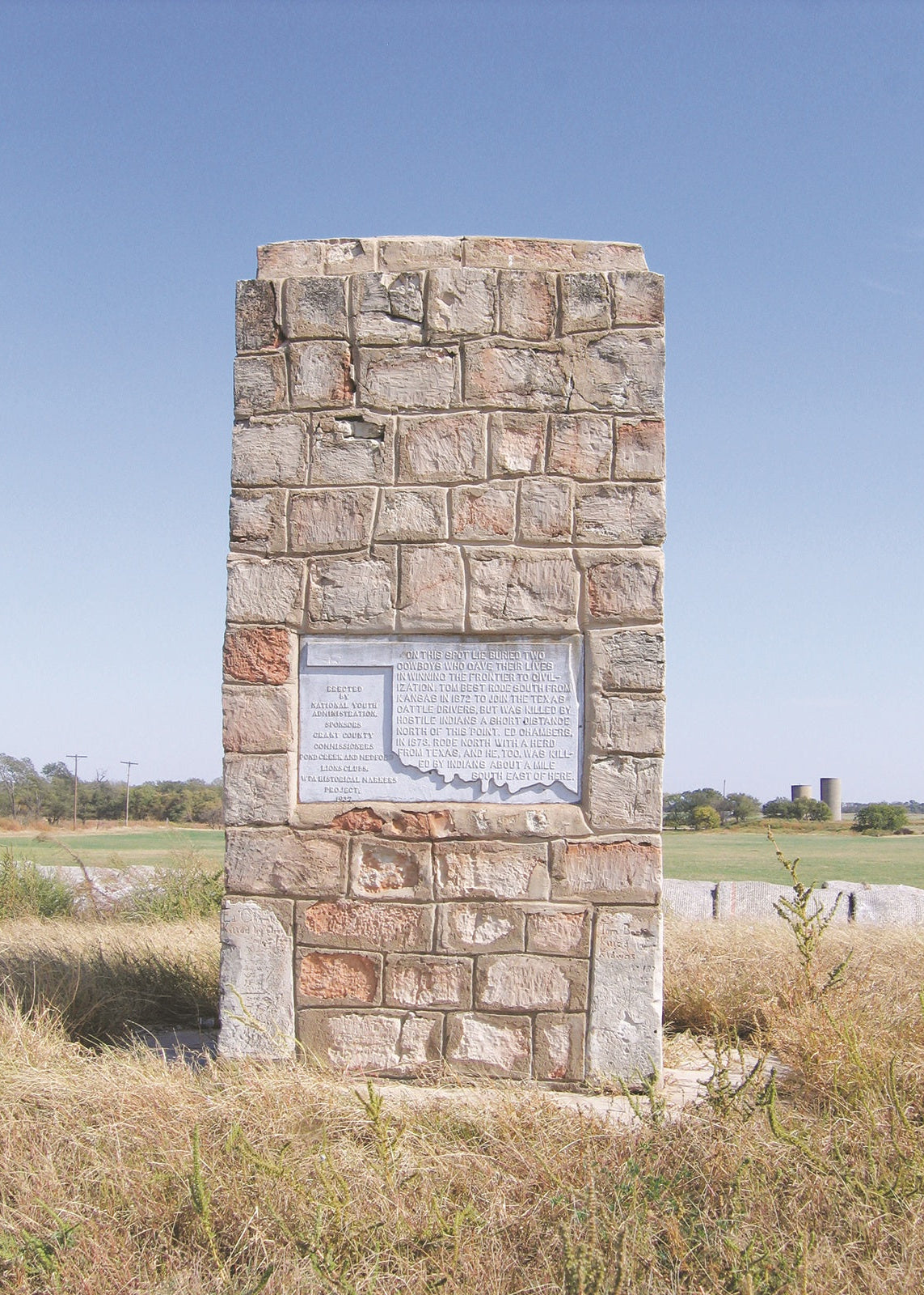 Stone monument with an engraved plaque in a field under a clear blue sky, Oklahoma