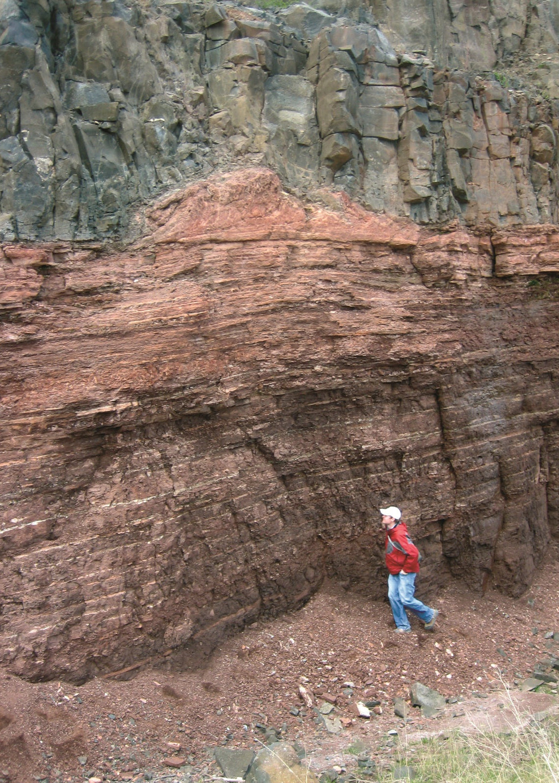 A gray basalt flow overlies an interflow sedimentary unit in a roadcut in Minnesota. There is a person in a red jacket at the base. 