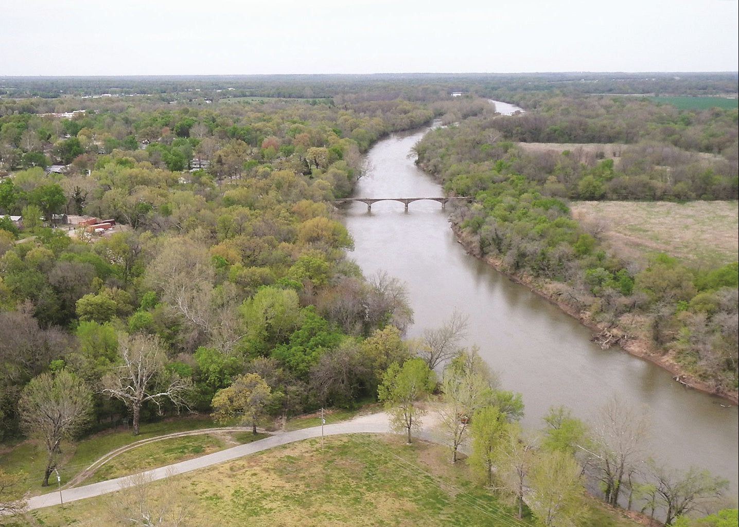 Aerial view of a river winding through a green landscape with trees and a road. Spring River, Kansas