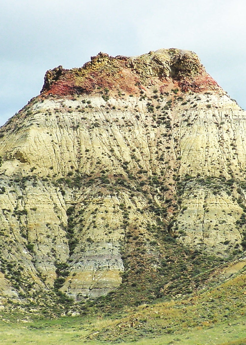 Tall, conical rock formation with a flat top in a grassy landscape. Clinker Cap, Montana
