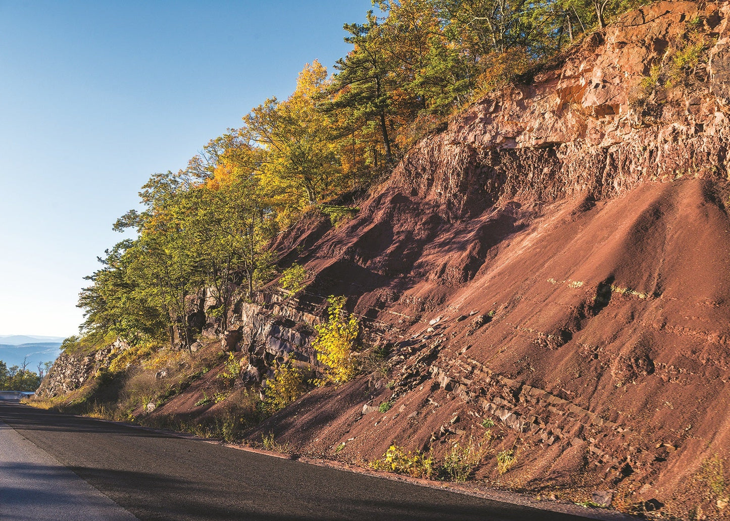 Roadside with a red cliff and trees on a clear day, West Virginia
