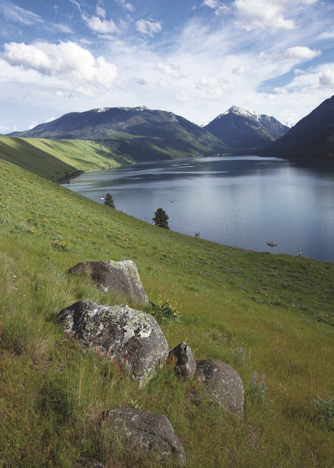 Wallowa Lake, Oregon, with grassy hillside in the foreground and mountain peaks and clouds in the background. 