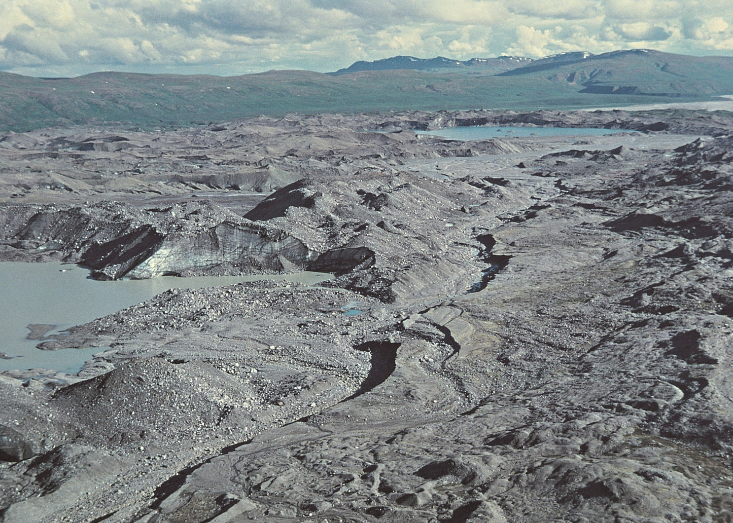 Vast volcanic landscape with lava flows and craters under a cloudy sky.