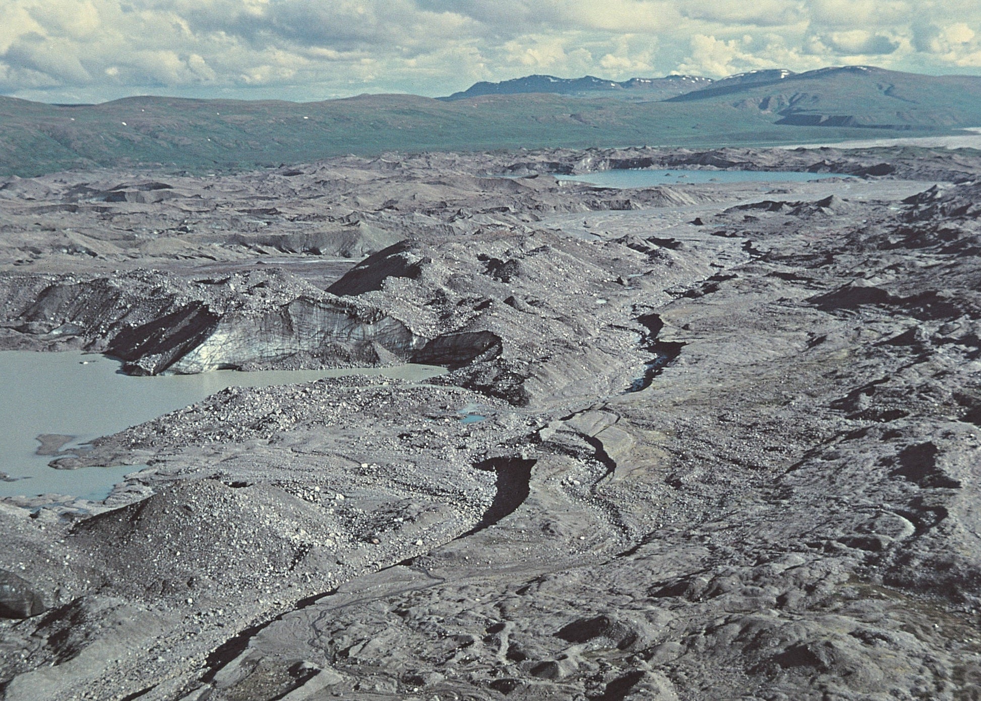 Vast volcanic landscape with lava flows and craters under a cloudy sky.