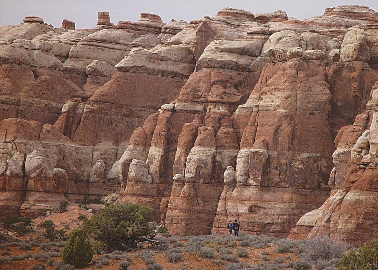 Rugged red rock formations in a desert landscape with two people walking, below. The Needles, Canyonlands National Park. 