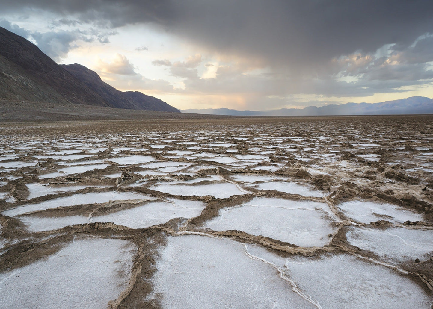 Desert landscape with salt flats and mountains under a cloudy sky. Badwater, Death Valley, California