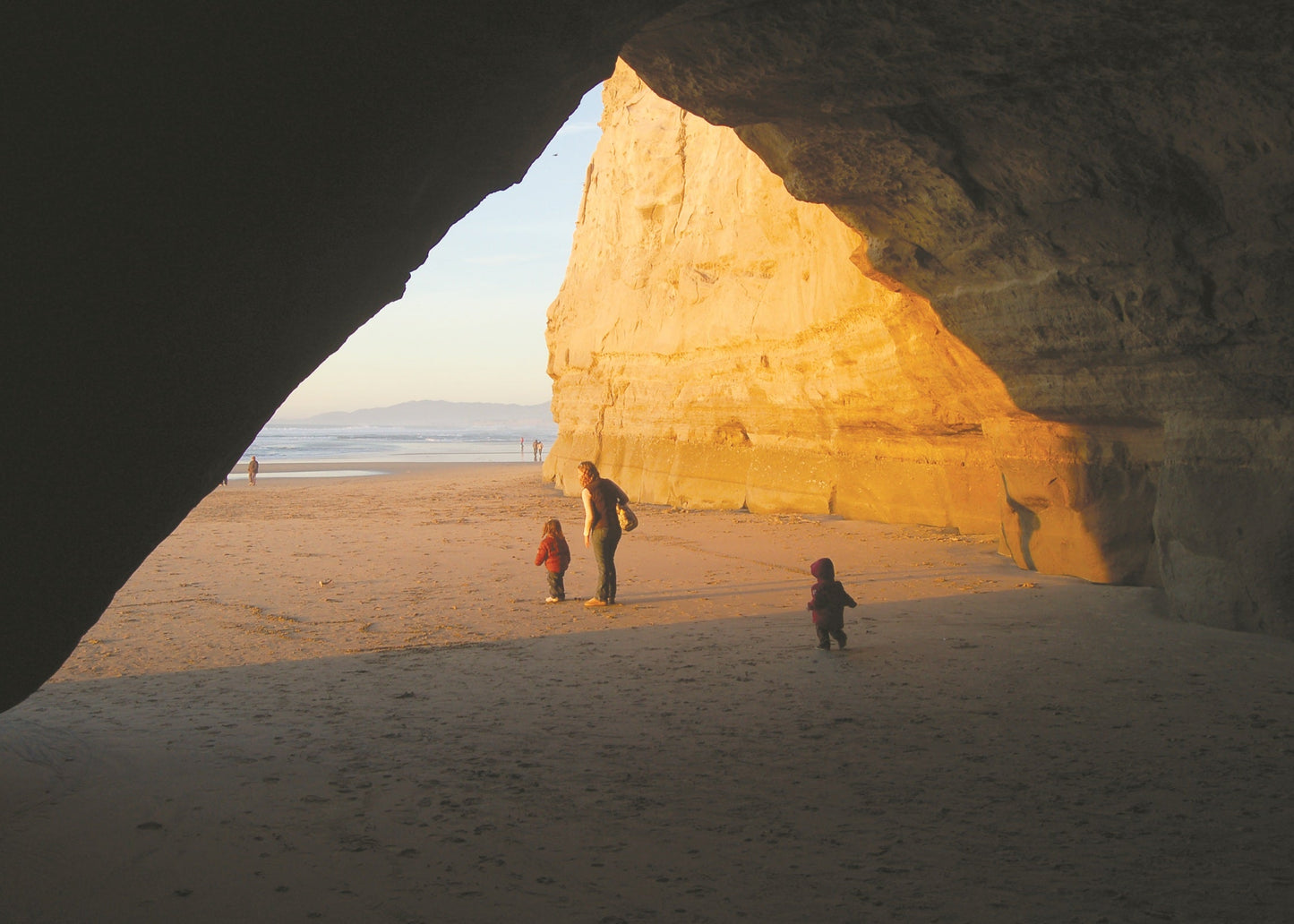 People exploring a large natural sandstone formation on a beach.