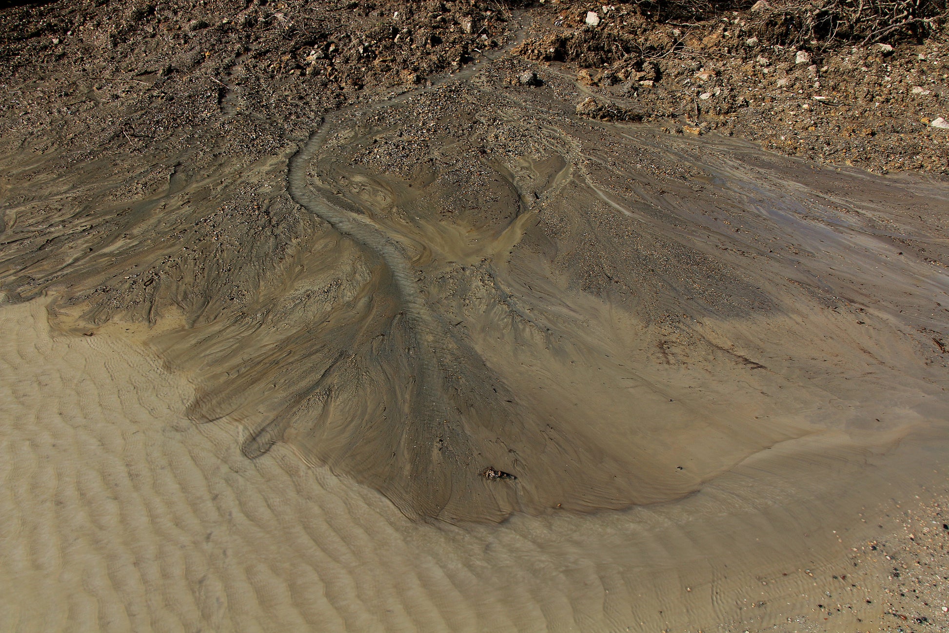 Alluvial fan stratigraphy image. Water flows over tannish-brown sand and rock.