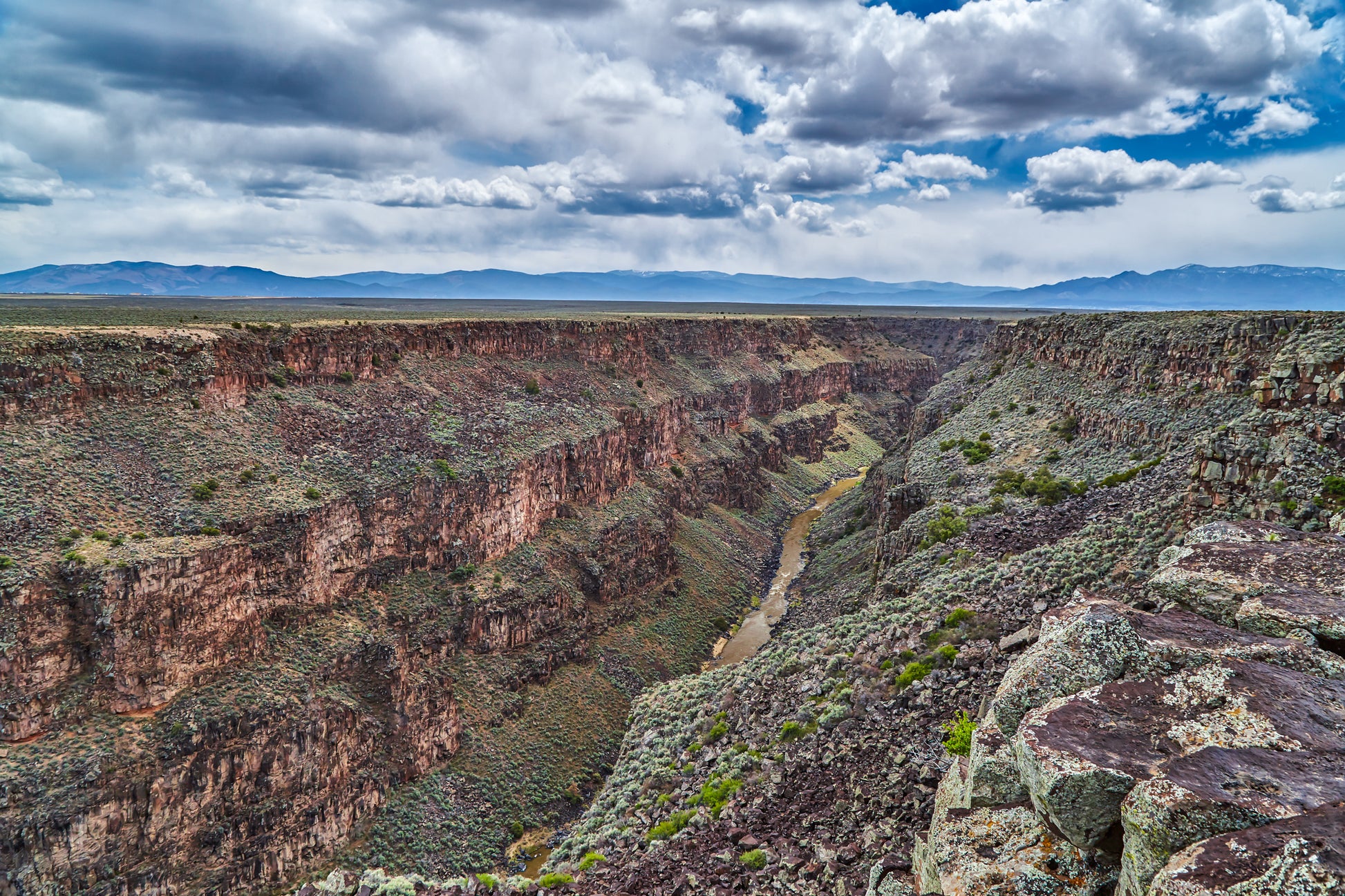 Superb rift basin-fill exposures. Wide-angle view of a canyon with a river running through it, under a blue sky with clouds.