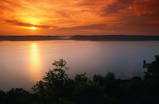 Sun sets over a large body of water surrounded by land and vegetation. Hydrogeology image.