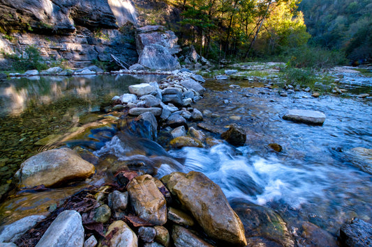 Water rushes over rocks in a riverbed surrounded by trees. Archaeology & Fluvial Landscapes image.