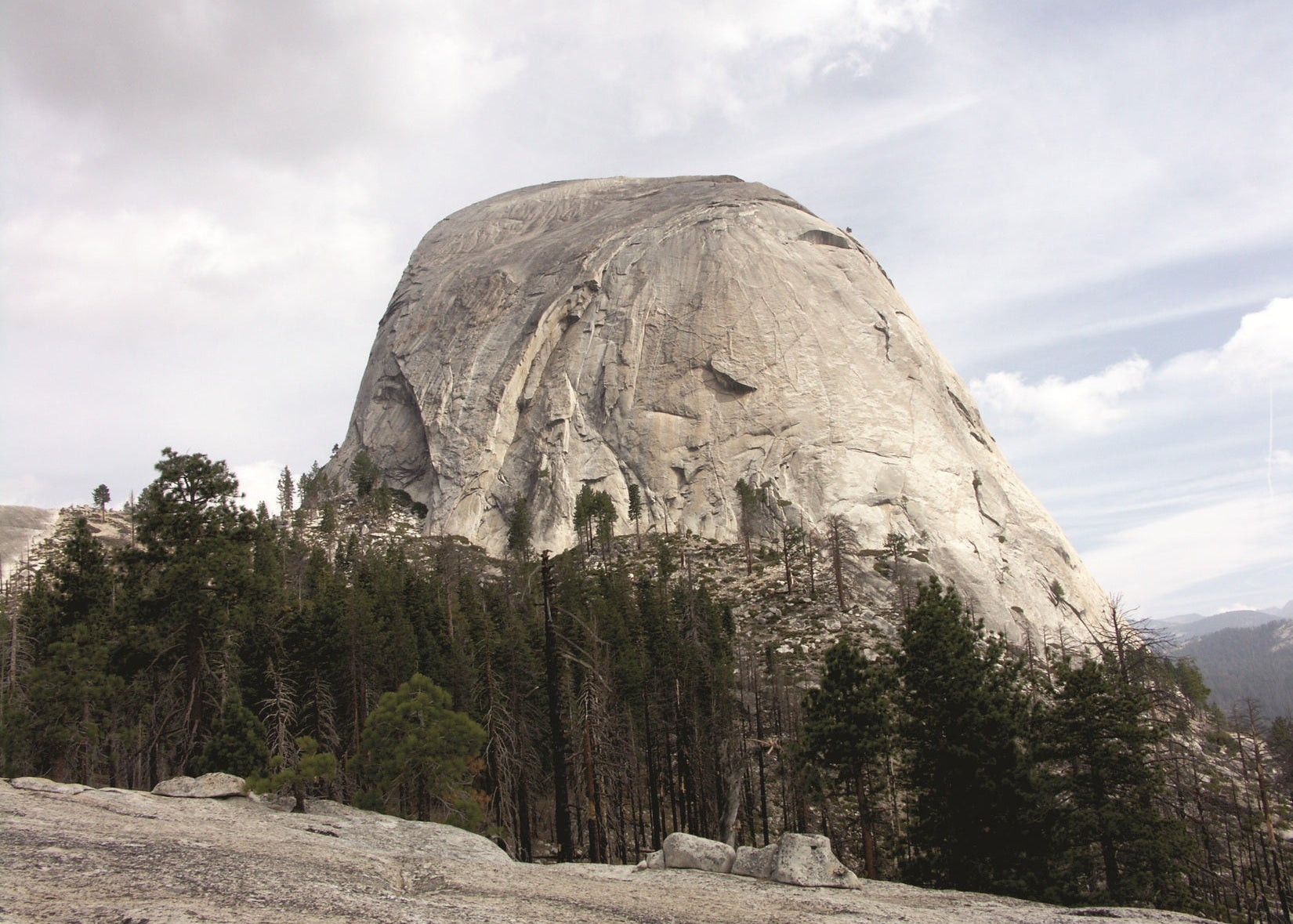 Half Dome, a large rocky outcrop with trees at its base under a cloudy sky. Yosemite 