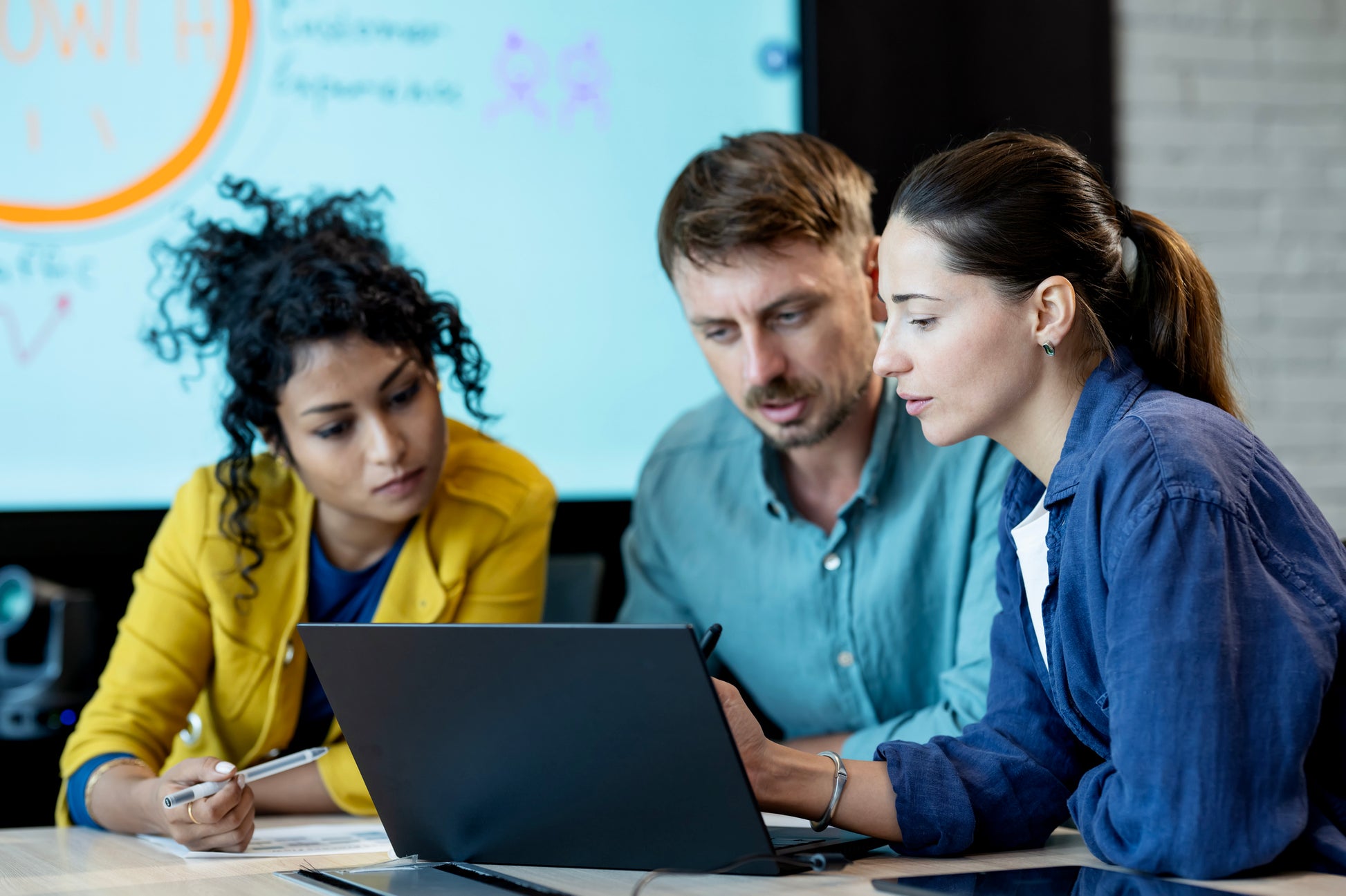 Three individuals sit and look at a laptop in front of them. Hands-on experience image.