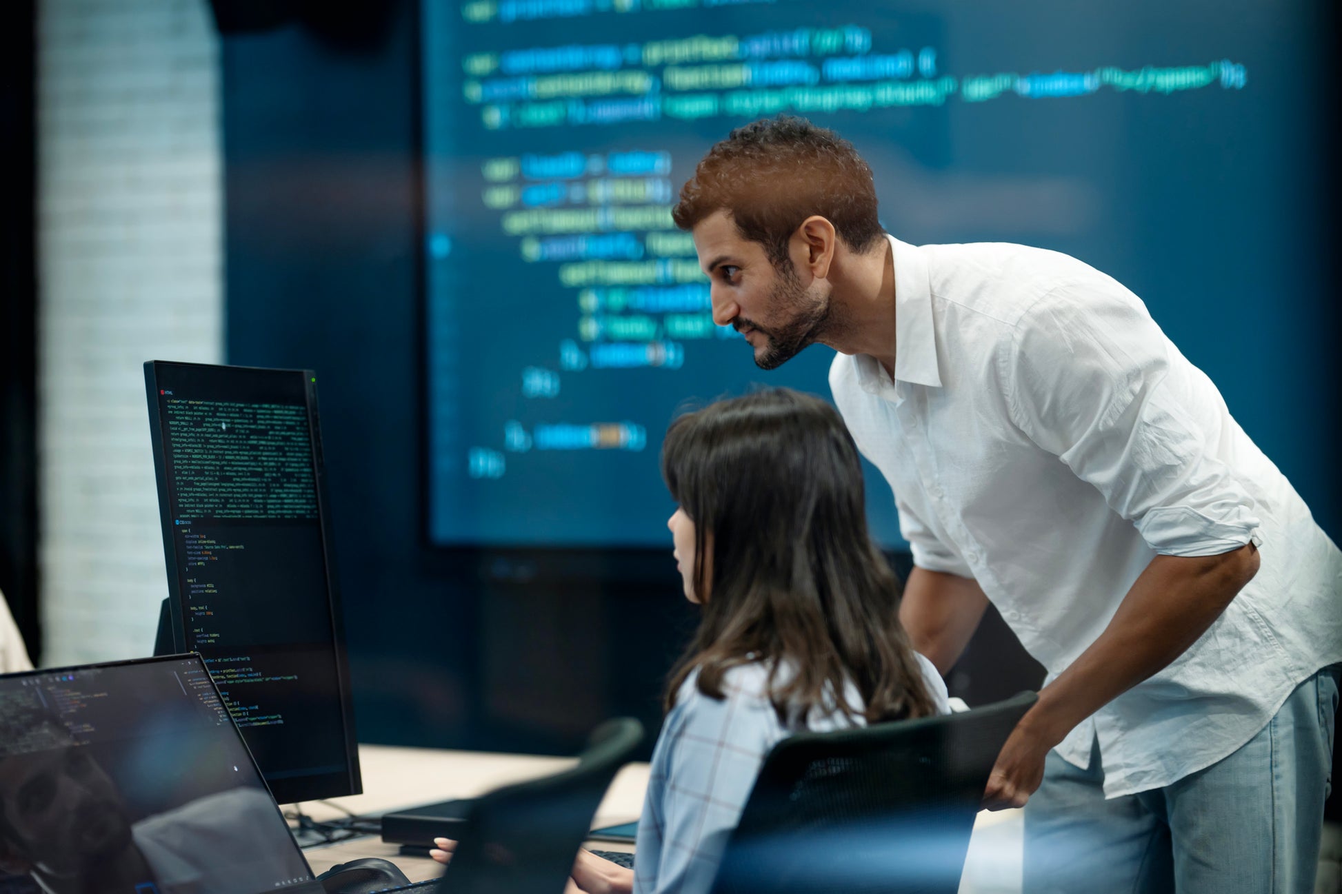 Two individuals in a learning environment look at a screen displaying code. Machine Learning image.