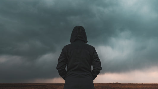 Person in a dark hooded jacket standing in front of a stormy sky. Climate Psychology image.
