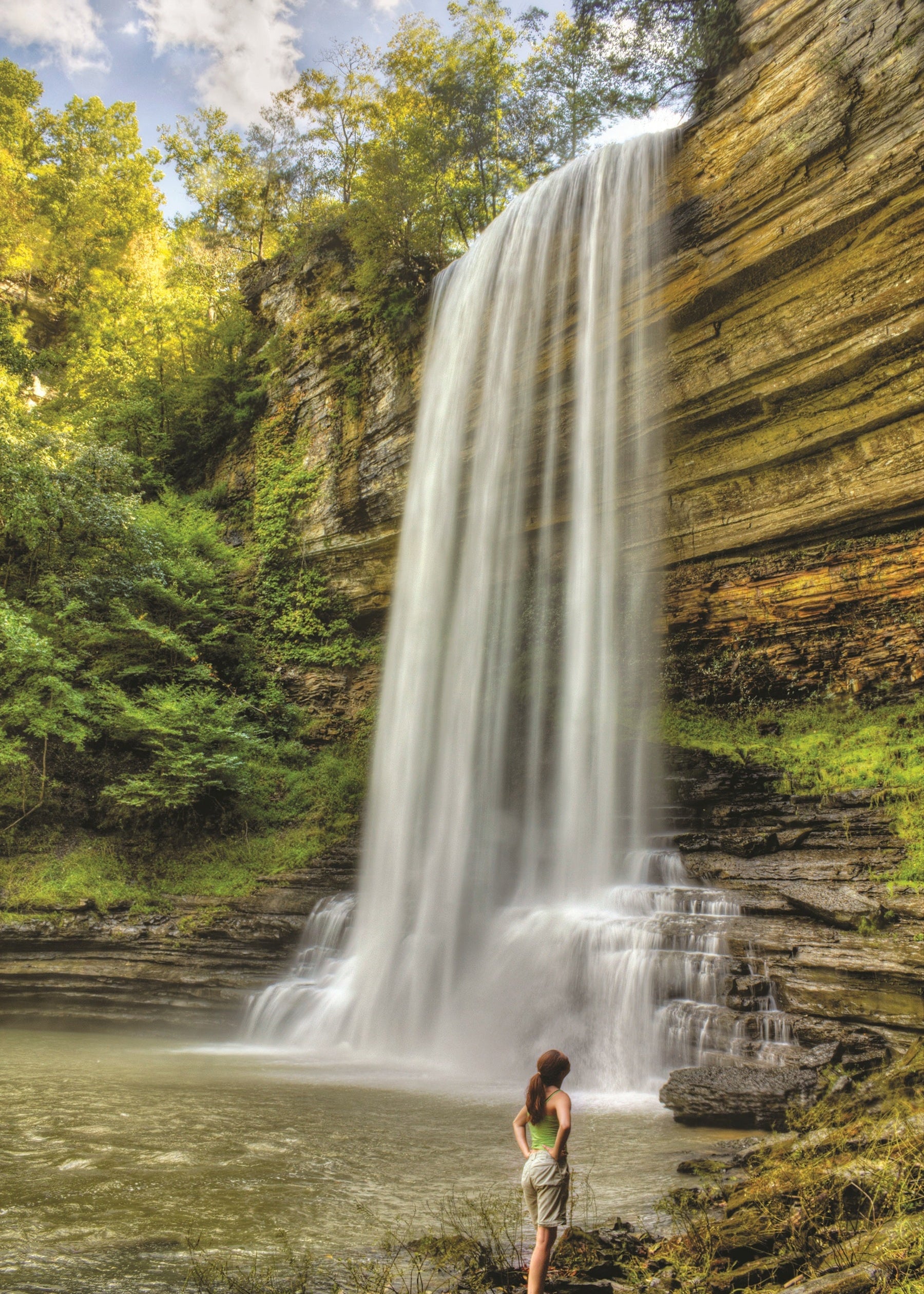 Woman standing at the base of a Fancher Falls in a forested area, Tennessee
